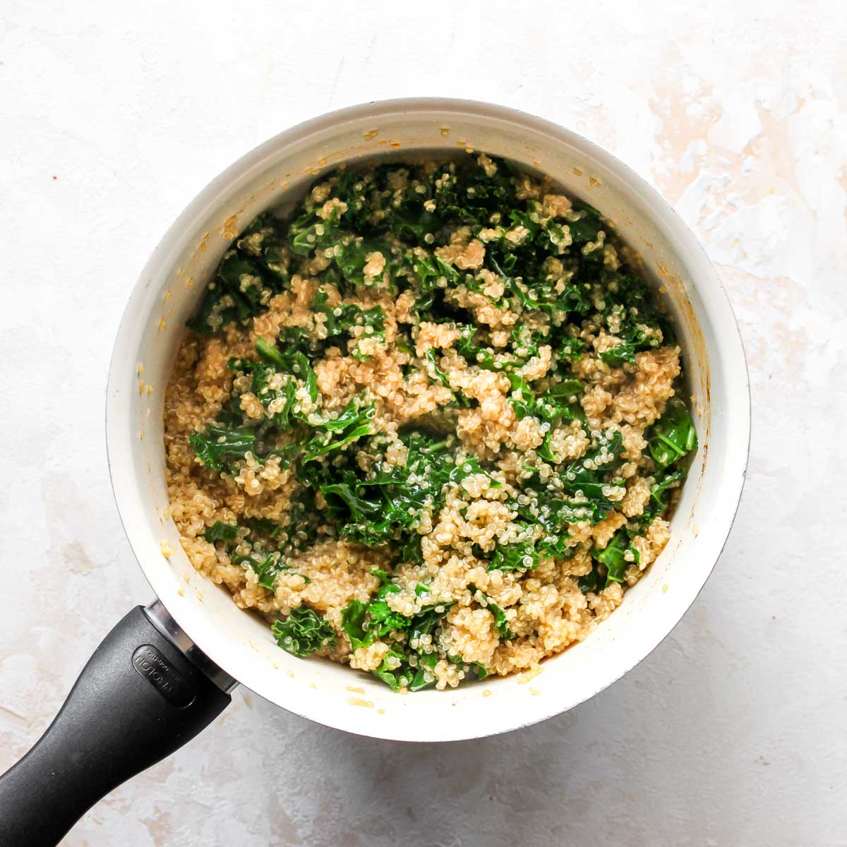 Cooked quinoa and kale steaming in a white saucepan