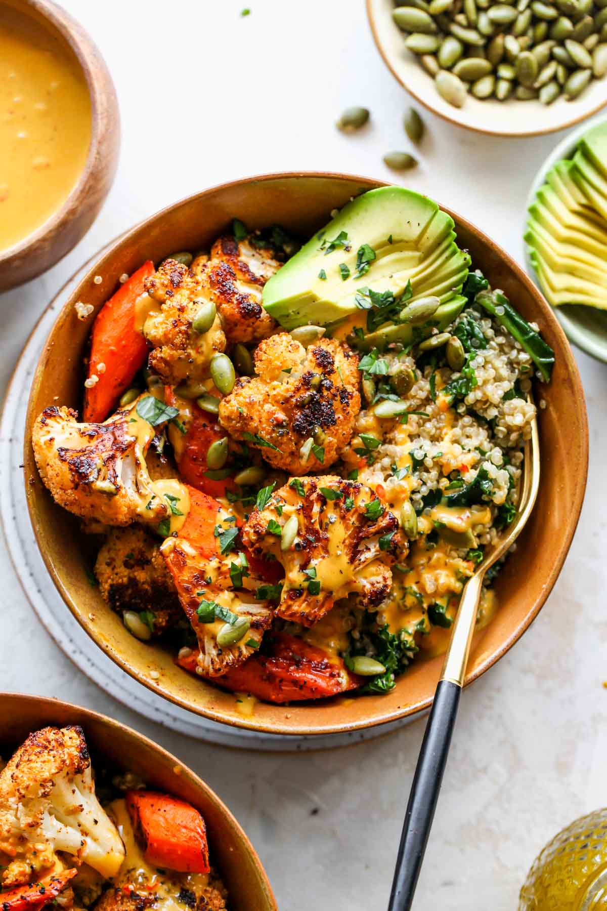 Vegan buddha bowl with grains, vegetables, and tahini sauce served in a gold bowl