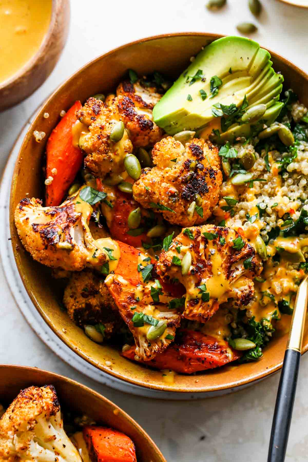 Roasted veggie buddha bowl topped with tahini sauce and avocado slices